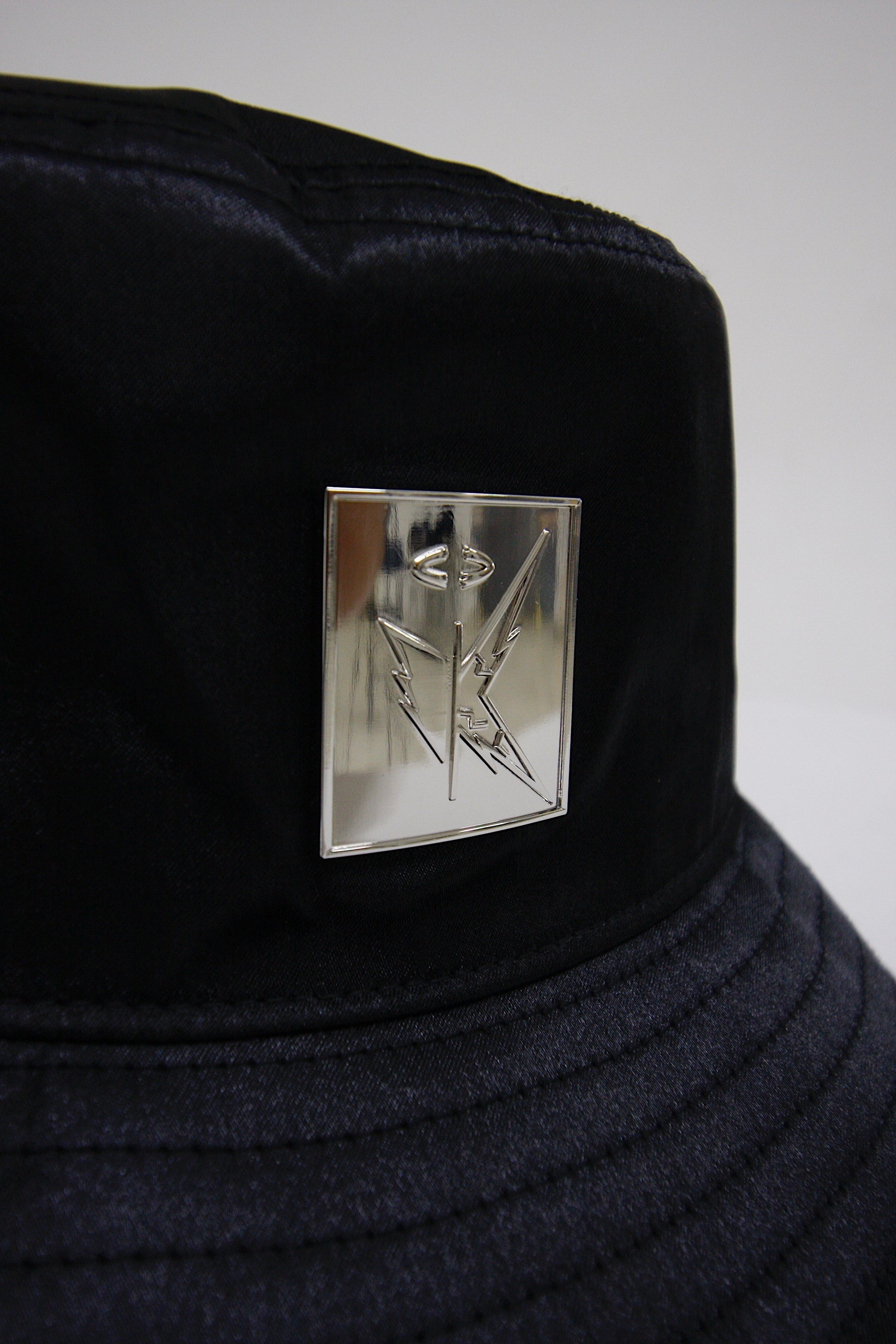 Streetwear inspired black satin bucket hat with silver EMLOTTI logo on front and back.